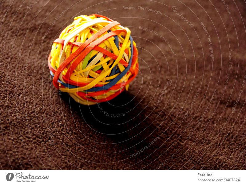 Das Objekt der Begierde - Ein Ball aus Gummibändern auf einer braunen Decke Haushaltsgummis Schwache Tiefenschärfe Farbfoto Menschenleer Nahaufnahme Kugel bunt