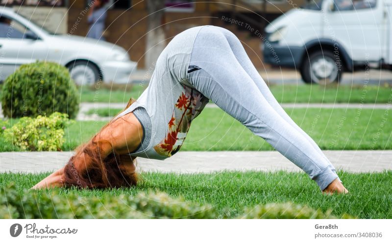 junges Mädchen in Yoga-Pose auf grünem Gras auf dem Rasen auf dem Straßenhintergrund der Stadt Erwachsener hell Sträucher Autos Großstadt Stadtstraße Tag Übung