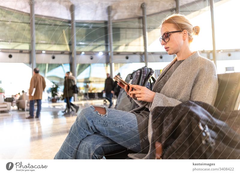 Eine weibliche Reisende, die ihr Handy benutzt, während sie an den Abfluggates im Flughafen-Terminal auf das Einsteigen in ein Flugzeug wartet. reisen Telefon