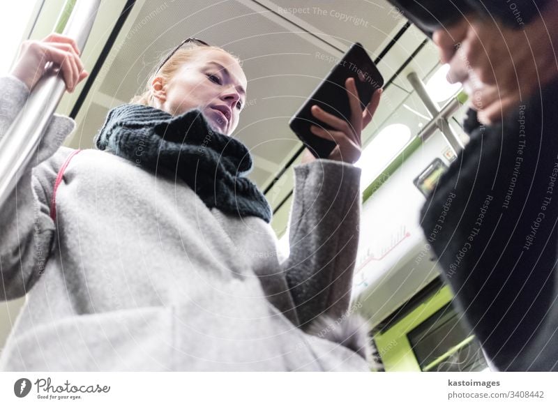 Schöne blonde Frau in Wintermantel und Schal, die während der Fahrt mit den öffentlichen Verkehrsmitteln der U-Bahn am Telefon liest. Großstadt Passagier urban