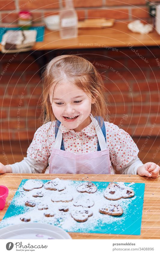 Kleines Mädchen glücklich wegen ihrer gebackenen Kekse. Kekse mit bunten Streuseln und Puderzucker dekorieren. Kind nimmt am Backworkshop teil. Backkurse für Kinder, aufstrebende kleine Köche. Kochen lernen. Kombinieren und Rühren von vorbereiteten Zutaten.