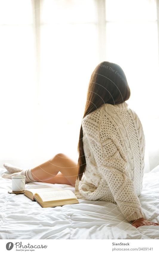 Weiches Foto einer Frau auf dem Bett mit einem alten Buch und einer Tasse Kaffee lesen Fenster Ansicht LAZY Sonntag Winter Tee Morgen Mädchen heimwärts