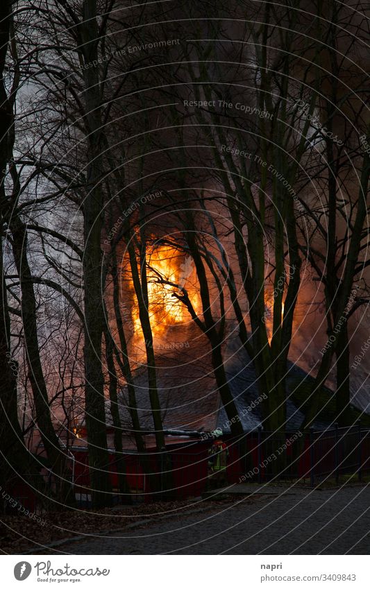 Flammen lodern aus dem Dach eines brennenden Gebäudes. Brand Feuer Haus Feuerwehr Feuerwehrmann Rauch bedrohlich gefährlich Unglück löschen Katastrophe Bäume
