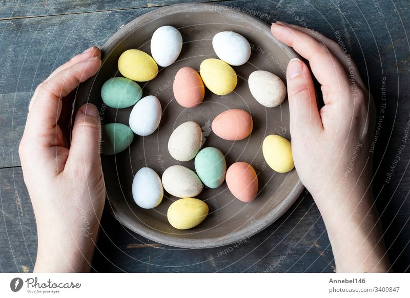 Hände halten stilvolle, pastellfarben bemalte Ostereier in grauer Keramikplatte auf altem Holzgrund, Fröhliche Ostern Feiertag Frühling traditionell Ei Symbol