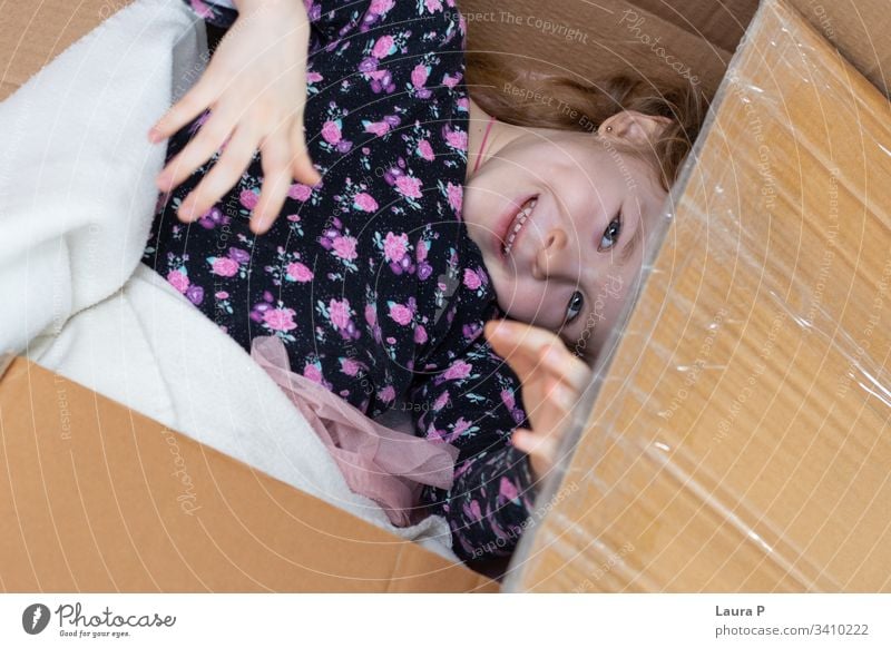 Kleines blondes Mädchen, das sich in einem Pappkarton versteckt einen Blick in die Tasche werfen Versteckspiel Familienspaß Fröhlichkeit Glück genießen Lachen
