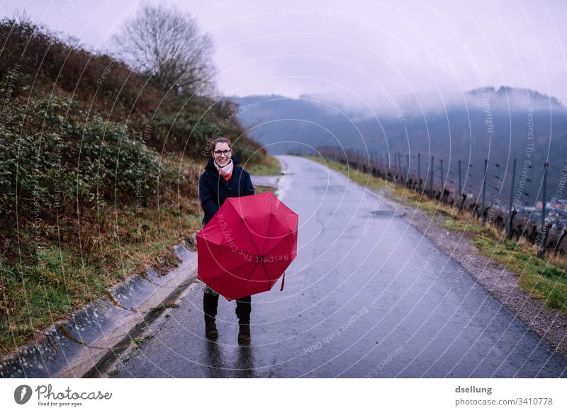 Regenspaziergang einer jungen Frau mit rotem Regenschirm Regentag regen nass schlechtes Wetter Farbfoto Außenaufnahme Lächeln Schirm Nebel Schutz Freude Straße