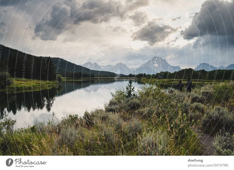 Spiegelglatter See mit grünen Wäldern an den Ufern und steilen Schneebedeckten Bergen im Hintergrund authentisch Nationalpark Yellowstone Nationalpark Himmel