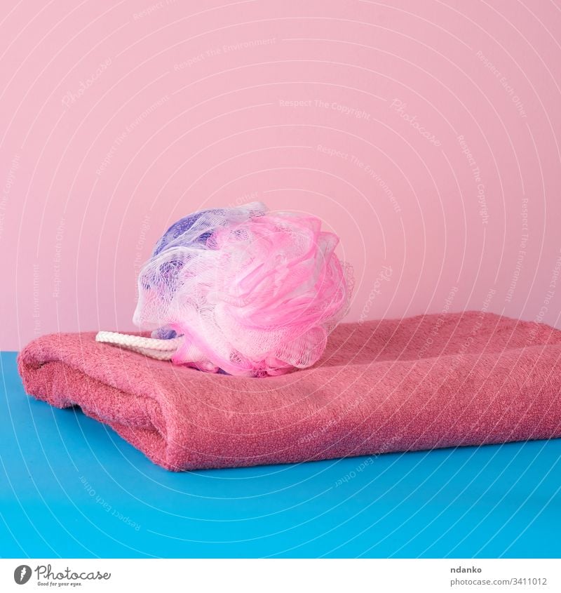 Stapel von rosa gefalteten Handtüchern und einem Plastikwaschlappen auf blauem Hintergrund Bad Schönheit Körper hell Pflege Sauberkeit Nahaufnahme Stoff Farbe