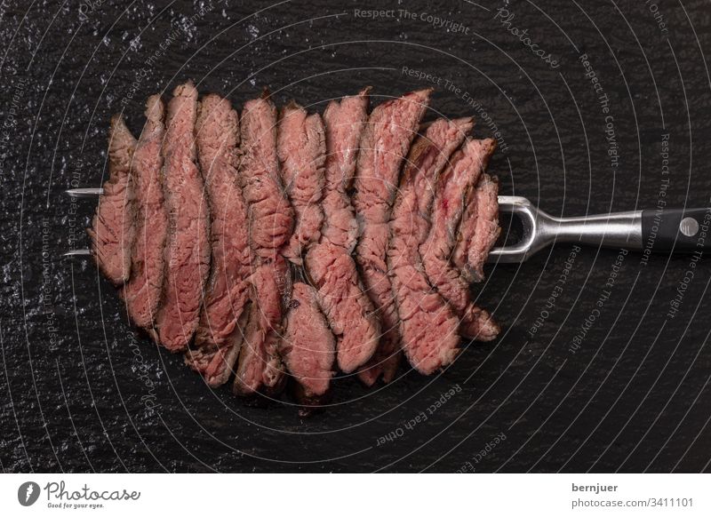 Scheiben eines Steaks auf Schiefer Rindersteak Fleischgabel Metzger Barbecue Aufsicht Fett gegrillt medium geschnitten Gabel Rindfleisch roh fettarm schwarz rot