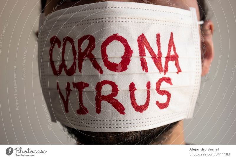 Einem CORONAVIRUS-Patienten mit Bart wurde eine weiße Gesichtsmaske mit roter CORONAVIRUS-Beschriftung angelegt. Konzept-Fotografie COVID-2019 2019-ncov wach
