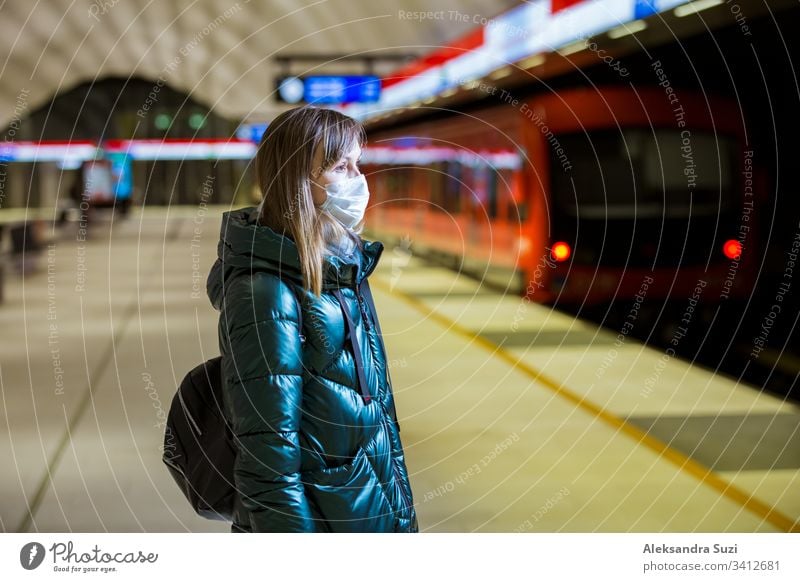 Frau im Wintermantel mit Schutzmaske auf dem Gesicht in der U-Bahn-Station stehend, auf den Zug wartend und besorgt schauend. Präventivmaßnahmen an öffentlichen Plätzen von Epidemiegebieten. Finnland, Espoo