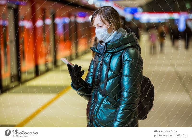 Frau im Wintermantel mit Schutzmaske auf dem Gesicht in der U-Bahn-Station stehend, auf den Zug wartend und besorgt schauend. Präventivmaßnahmen an öffentlichen Plätzen von Epidemiegebieten. Finnland, Espoo