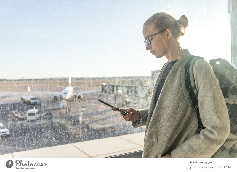 Lässig gekleidete Reisende auf dem Flughafen, die auf ein Smartphone vor den Fenstern des Flughafens mit Blick auf die Flugzeuge auf der Startbahn schaut reisen