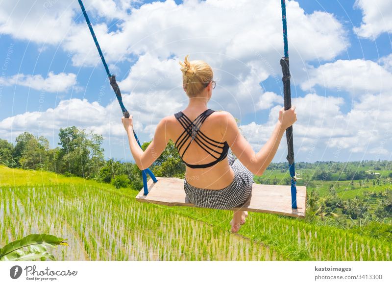 Eine glückliche Reisende, die auf einer Holzschaukel schaukelt und ihren Sommerurlaub inmitten unberührter grüner Reisterrassen genießt. pendeln Frau frei Natur
