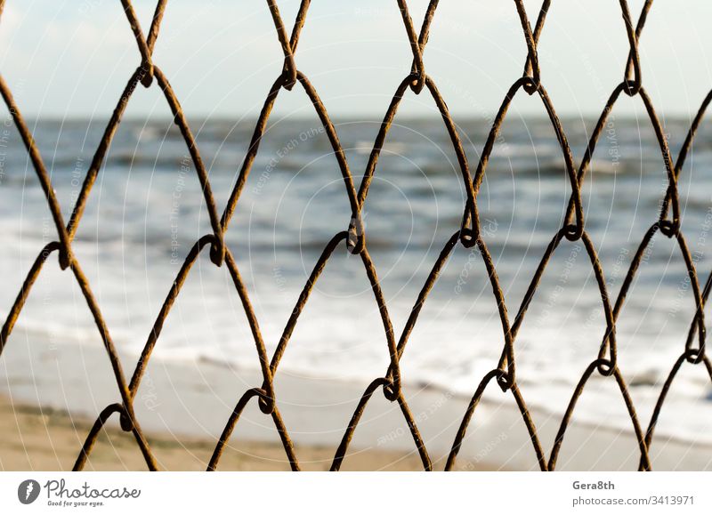 Maschendrahtzaun auf dem Hintergrund des Strandes und des Meeres abstrakt Unschärfe verschwommen Zaun ineinander greifen Natur Wiederholung Rust rostig Sand