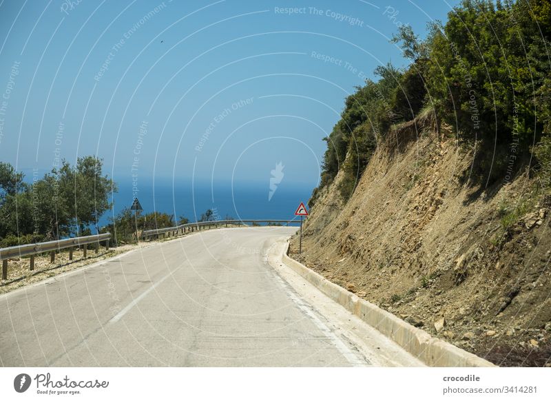 kurvige Küstenstrasse in Albanien die nach rechts abzweigt Straße albanien Kurve Schilder & Markierungen Beton alt Meer roadtrip Büsche Asphalt Linie