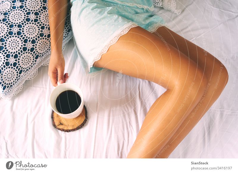 Junge Frau genießt ihren Kaffee im Bett sitzend. gemütlich Morgen Tasse Mädchen heimwärts Buch Beine weich Socken Top Ansicht jung warm Schlafzimmer schön weiß