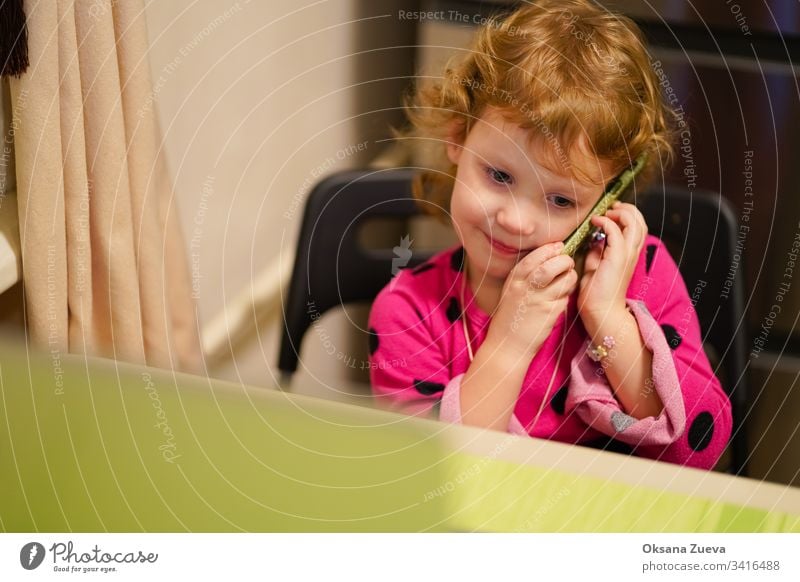 Das gelockte kleine Mädchen spricht mit seiner Großmutter am Telefon. Sie lächelt, erzählt den Nachrichten, wie es ihr geht. bezaubernd attraktiv Baby schön
