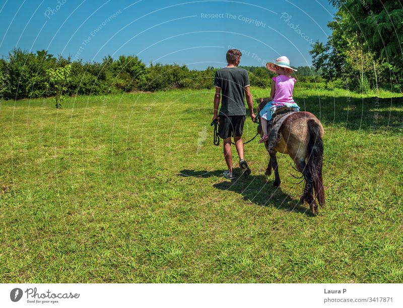 Kleines Mädchen reitet im Sommer auf einem Pony auf einer grünen Wiese Aktivität Tier auf dem Land auf dem Bauernhof schön züchten Pflege Kind Kindheit