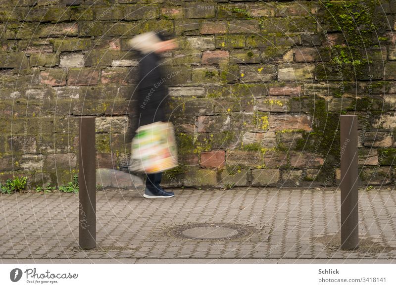 Mensch oder Außerirdischer mit bunter Plastiktüte geht vor schmutziger Wand Bewegungsunschärfe gehen Mann Pfosten Langzeitbelichtung Gully Gullydeckel