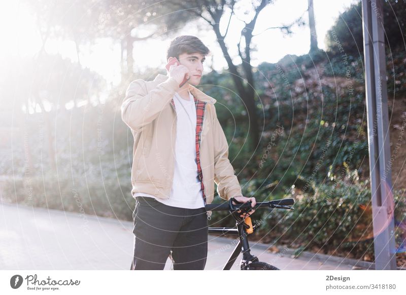 Junger hispanischer Mann, der ein Handy benutzt und ein Fahrrad mit sich führt, wenn er im Freien geht Beteiligung jung 1 Glück Gesicht Person männlich cool