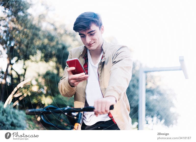 Junger, gutaussehender Typ auf dem Fahrrad, der auf ein Mobiltelefon schaut. 1 Telefon Lifestyle Technik & Technologie Mobile Stil Großstadt Mann jung Rad