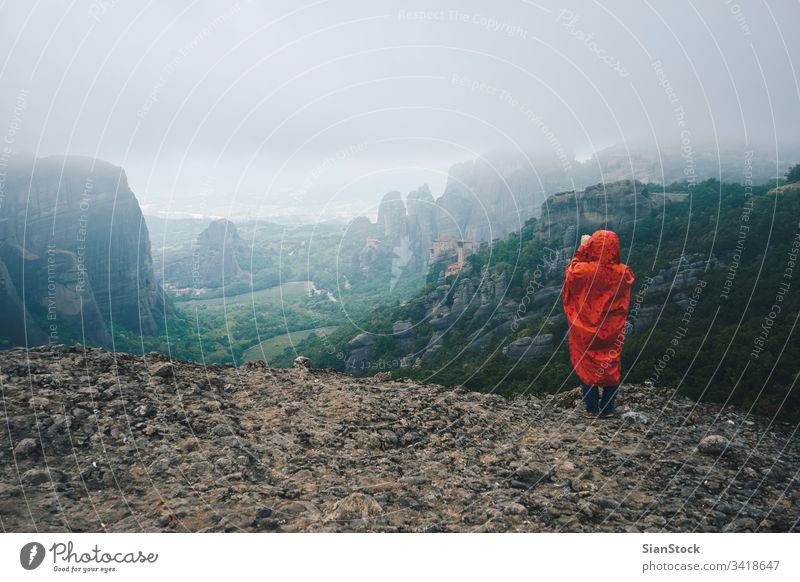 Frau mit rotem Regenmantel fotografiert mit ihrem Smartphone die Landschaft der Meteora-Felsen, Griechenland Kloster Nebel Berge u. Gebirge wandern Tour