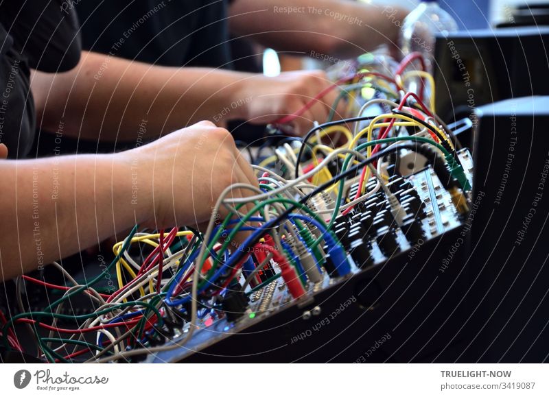 DJ Equipment Electro Mischpult für elektronische Musik mit vielen Reglern, bunten Kabeln und Steckern wird von zwei Händen gerade gesteuert elektronische musik