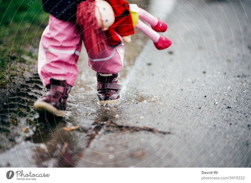 Mädchen Kind läuft mit Puppe durch Pfütze an einer Straße entlang nass gefährlich autoverkehr laufen unsicher Kleinkind Gefahr schlechtes Wetter Herbst
