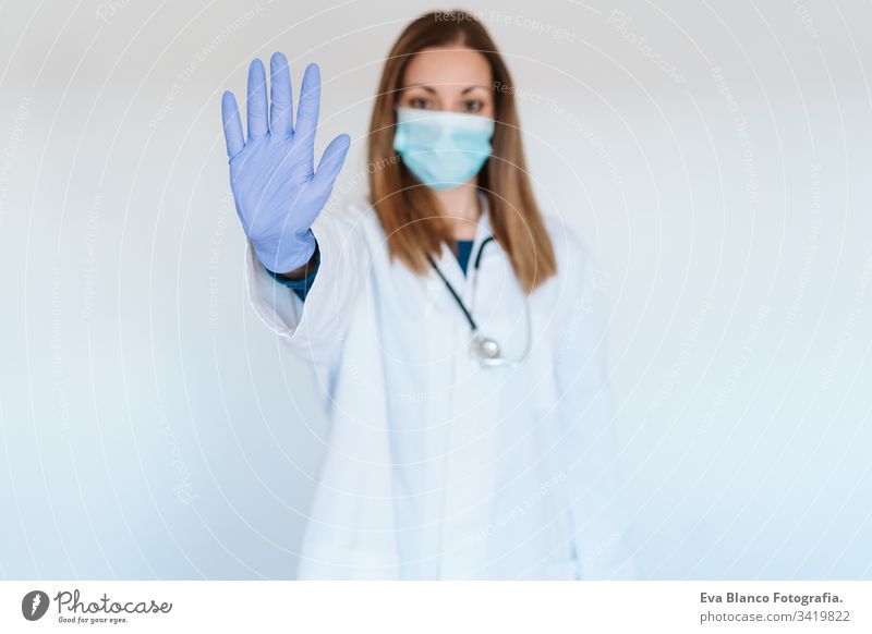 Porträt einer Ärztin, die im Haus eine Schutzmaske und Handschuhe trägt. Mit der Hand ein Stoppschild machen. Konzept des Coronavirus Frau stoppen Arzt