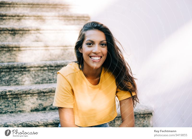 lateinamerikanisches Mädchen, das auf der Treppe sitzt und lächelt 20s Erwachsener attraktiv schön Schönheit Brasilien brünett sorgenfrei lässig heiter