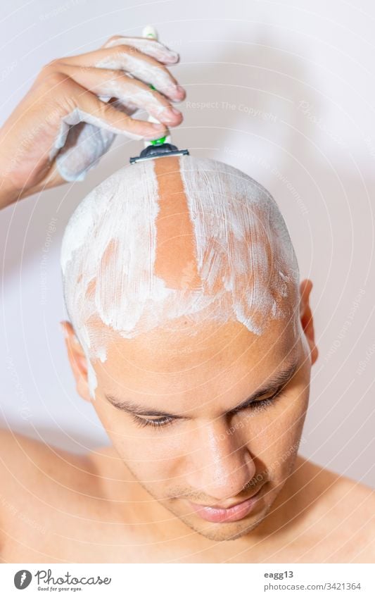 Mann rasiert seinen Kopf mit weißem Schaumstoff Vorschein kahl kahl werdend Bad Klinge Pflege Konzentration abgeschnitten Enthaarung Tatkraft Ausdrücken Auge
