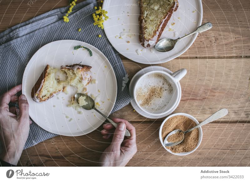 Anonyme Frau frühstückt mit köstlichem frischen Kuchen Dessert Zitrone Kokosnuss Scheibe Spielfigur Tasse Kaffee Tisch Teller Hand Arme hölzern Bestandteil