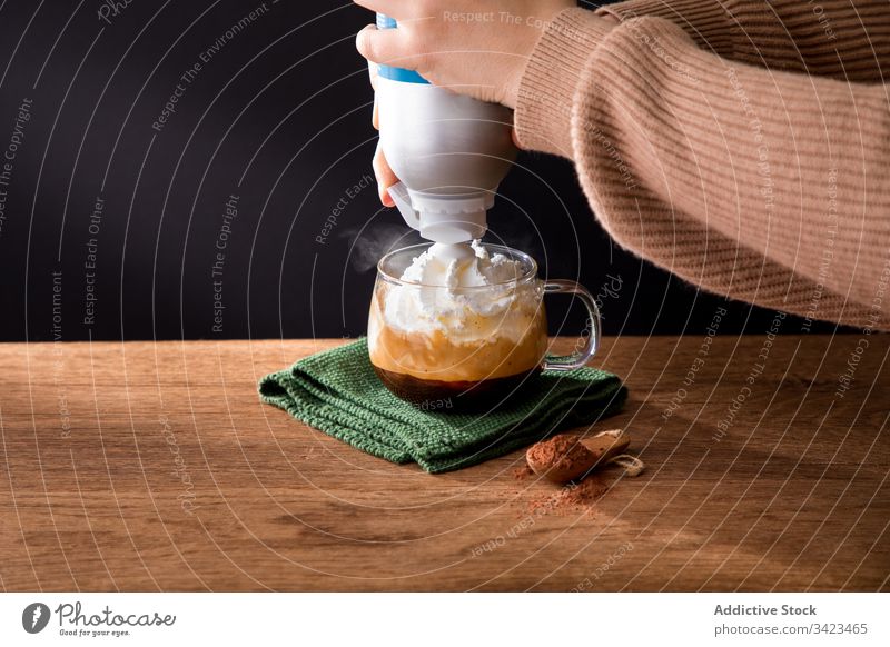 Frau gießt Schlagsahne in Kaffee gepeitscht Sahne vorbereiten eingießen Zimt Tasse trinken heiß frisch Hand Getränk lecker geschmackvoll Glas braun Tisch