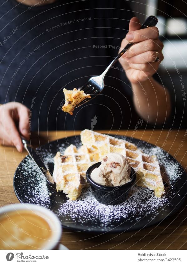 Anonyme Person, die in der Nähe von Kaffee Waffeln mit Eis isst Speiseeis Café essen geschnitten süß Tisch sitzen Gabel Messer lecker Lebensmittel geschmackvoll