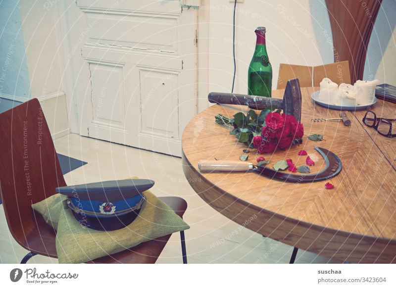 hammer und sichel liegen auf einem tisch, nebst geleerter weinflasche, einem strauß roter rosen und einer militärmütze Fotochallenge Hammer Sichel Tisch Küche