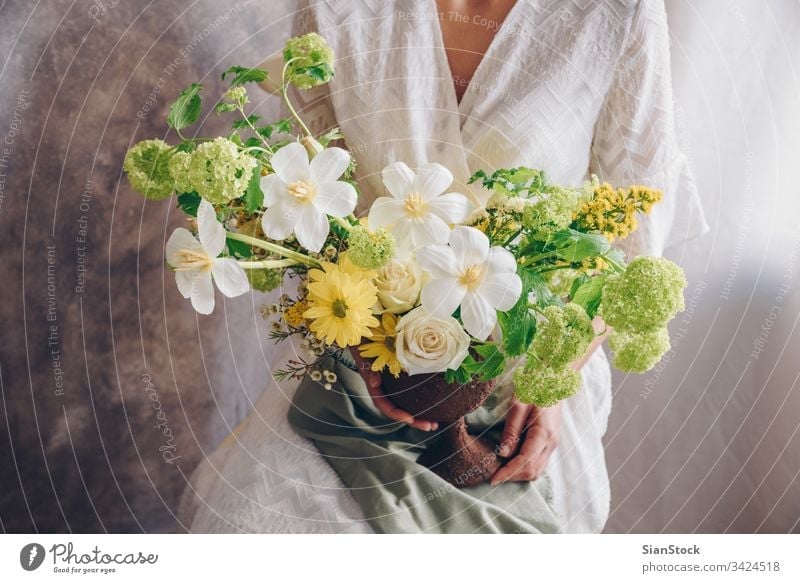 Junge Frau in einem weißen Kleid, die eine Vase mit Blumen hält. Vintage, romantisches Konzept. Blumenstrauß Mädchen Metall sitzen Sitzen Stuhl weiches Licht