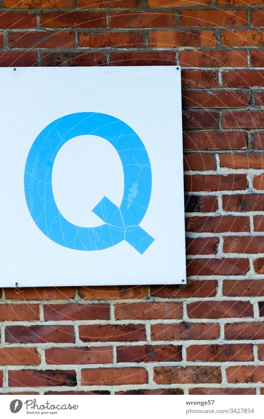 Blaues Q auf weißer Tafel an einer Backsteinmauer Buchstaben Farbfoto Tag Schriftzeichen Außenaufnahme Großbuchstabe blau Schild Ziegelmauer Gebäude Gebäudeteil