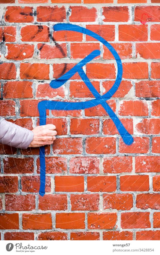 Eine Frauenhand hält scheinbar einen Hammer und eine Sichel - Graffito vor roter Backsteinwand Graffiti Hand hammer und sichel Backsteinmauer Hochformat
