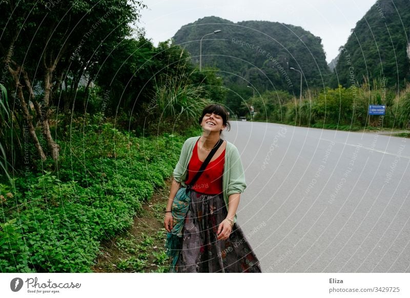 Eine junge Frau in bunter Kleidung, die eine leere Straße in Asien entlangläuft und lächelt Touristin Tourismus Südostasien Lebensfreude Reisen Urlaub