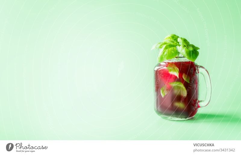 Limonade mit roten Beeren im Mason-Glas, gewürzt mit Kräuterblättern auf sonnig-hellem, minzgrünem Hintergrund. Sommerliche Stimmung.  Gesunde Getränke und Lebensweise. Raum kopieren