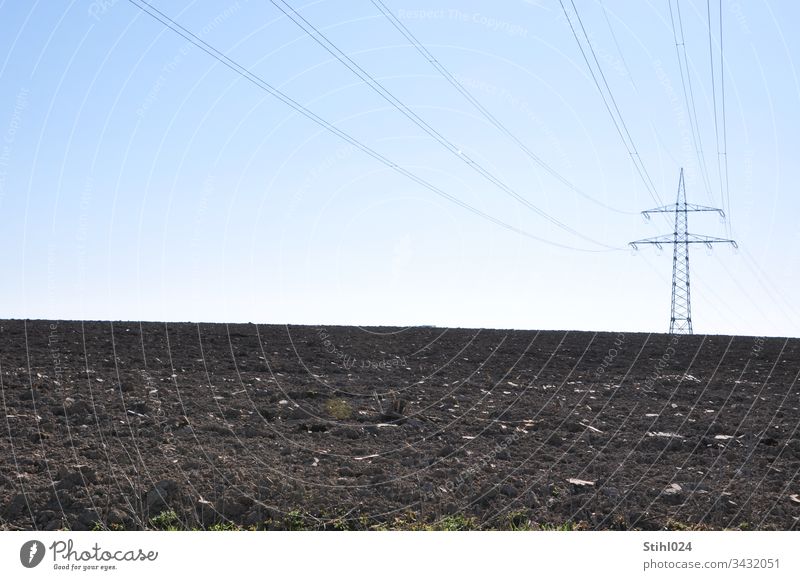 Hochspannungsmast steht auf Entfernung einsam auf gepflügtem Acker Strommast Stromversorgung Landwirtschaft Horizont Winter allein Trassenführung Landschaft