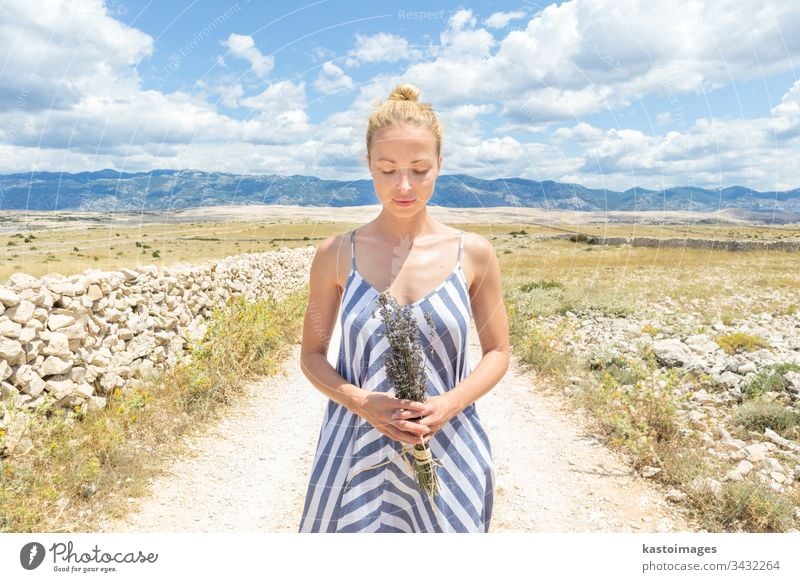 Kaukasische junge Frau in Sommerkleidung mit Lavendelblütenstrauß, die im Sommer die reine mediterrane Natur an der felsigen kroatischen Küstenlandschaft auf der Insel Pag genießt