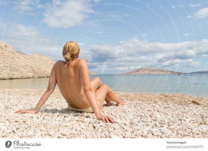 Rückansicht einer sexy jungen kaukasischen Frau, die sich oben ohne auf einem abgelegenen Pabble Beach auf der Insel Pag, Kroatien, im Mittelmeer sonnen. Strand