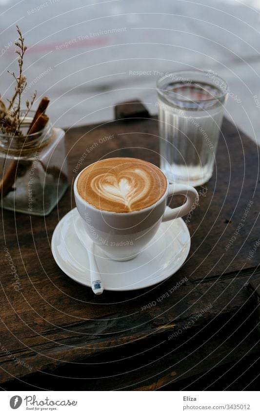 Eine Tasse Cappuccino mit einem Latte Art Herz auf einem Holztisch in einem Café Kaffee latte art Tisch TischHolztisch Getränk Frühstück braun Farbfoto Koffein