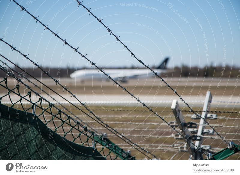 angestachelter Zaun hinter dem ein verschwommenes Flugzeug parkt Stacheldrahtzaun Außenaufnahme Flughafen Sicherheit Grenze Barriere Menschenleer Farbfoto