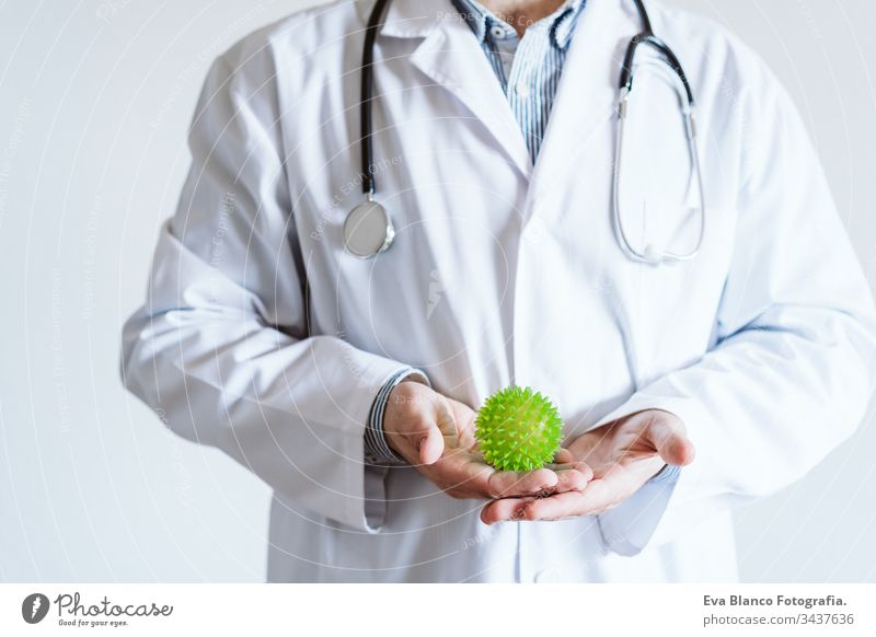 Ein Arzt, der im Haus eine Schutzmaske trägt. Er hält einen grünen Ball, der wie ein Coronavirus aussieht. Covid-19-Konzept Mann professionell Corona-Virus