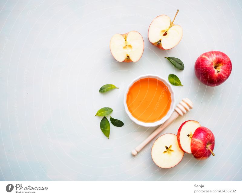 Roter halbierter Apfel und eine weiße Schüssel mit Honig auf einem hellen Hintergrund, Flachlage, gesunde Ernährung apfel verrotten honen honiglöffel draufsicht