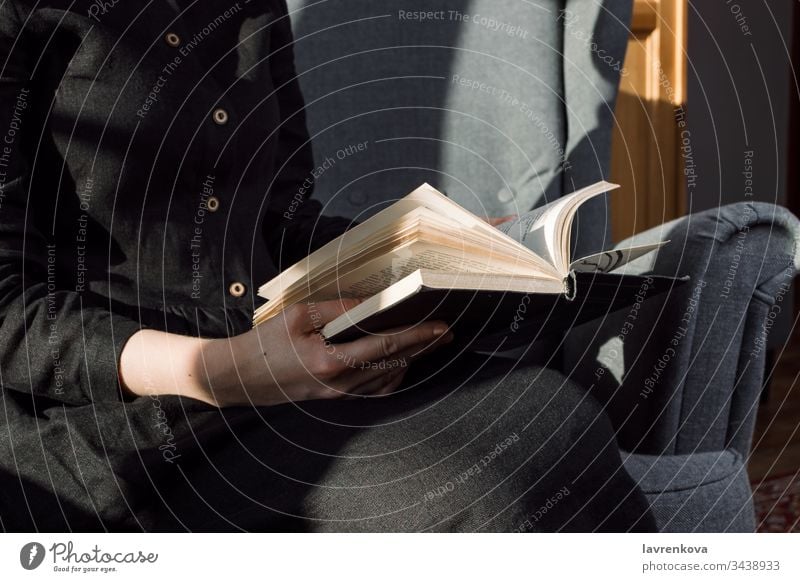 Nahaufnahme einer Frau in schwarzem Kleid, die ein Buch auf ihrem Schoss hält, selektive Fokussierung Bücher Stuhl gemütlich gesichtslos Finger Hände Hobby