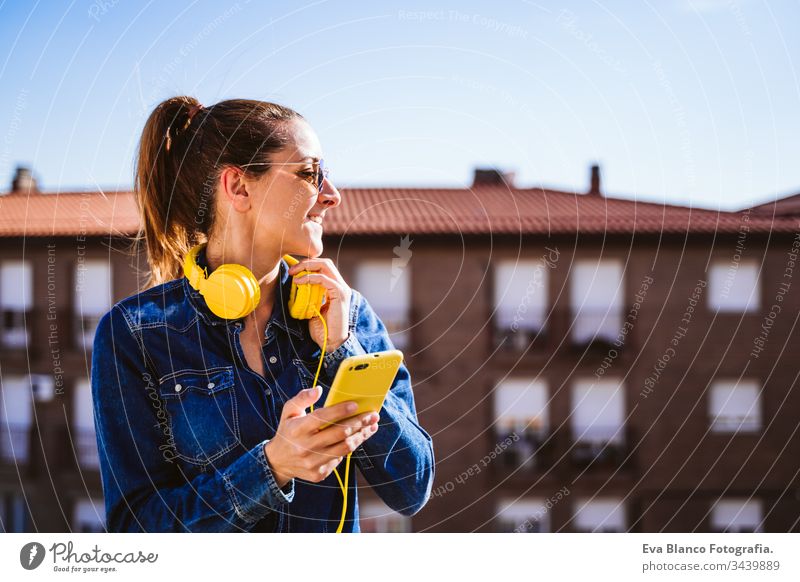 junge Frau, die über ein Mobiltelefon und ein gelbes Headset Musik hört. Spaß und Lebensstil hören Handy Technik & Technologie Terrasse im Freien sonnig